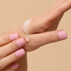 Hand with pink nail polish holding a dollop of cream against a beige background