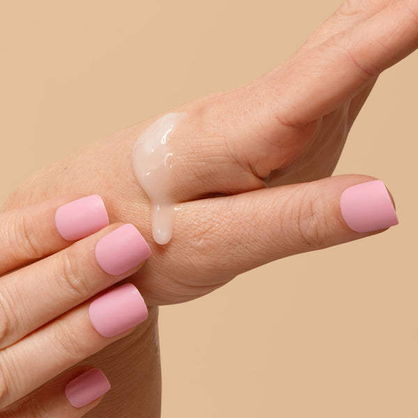 Hand with pink nail polish holding a dollop of cream against a beige background