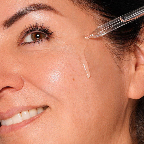 Close-up of a woman's face with a dropper applying a liquid to her skin.