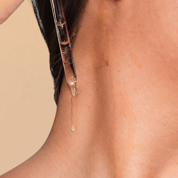 Close-up of a dropper applying a clear liquid to skin on a beige background