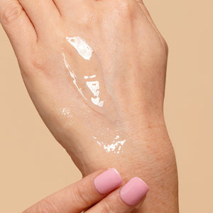 Hand with a small amount of white cream on a beige background